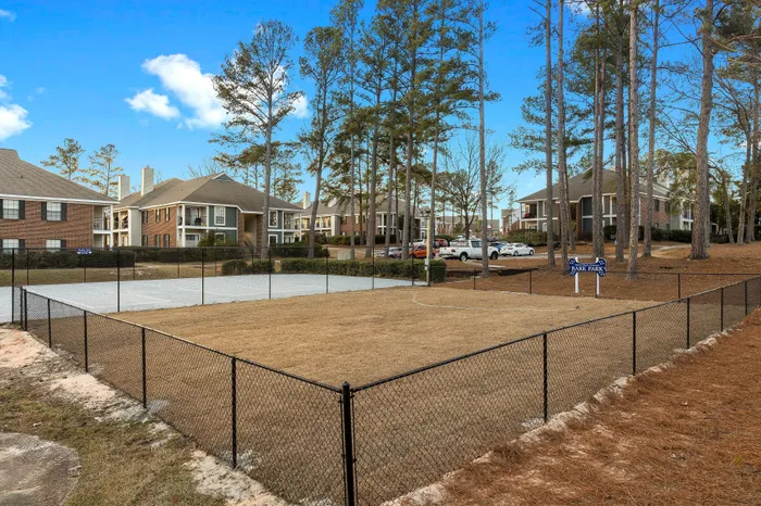 Charming apartment complex with spacious balconies, surrounded by tall trees and a fenced area ideal for outdoor activities.