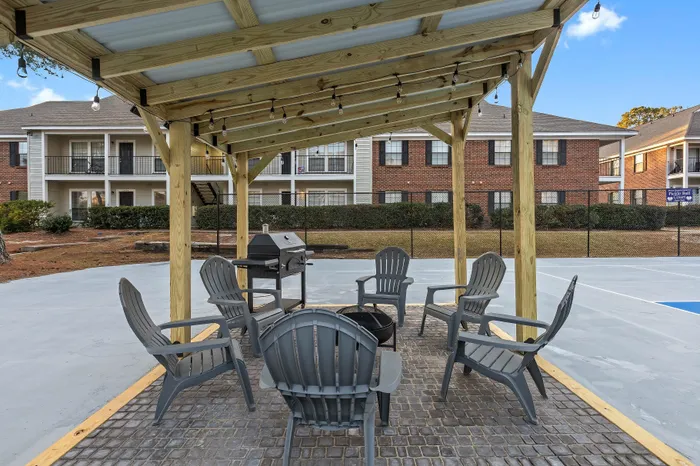 Inviting outdoor patio with modern seating and grill, nestled under a charming wooden pergola. Perfect for social gatherings in a serene apartment complex.