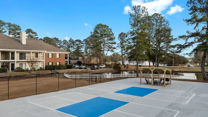 Charming outdoor community area with a covered seating space, surrounded by lush greenery and a peaceful pond, perfect for relaxation.