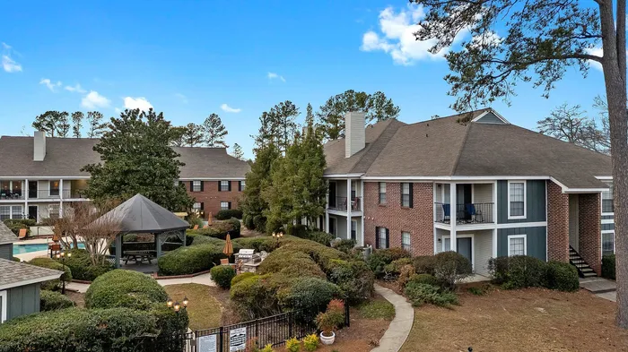 Charming apartment complex with lush gardens, a central gazebo, and inviting paths, offering serene living amidst nature.