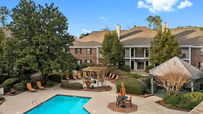 Charming apartment complex with a refreshing pool, lush landscaping, and cozy outdoor seating areas, creating a peaceful retreat for residents.