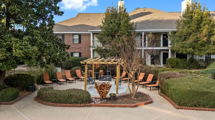 Charming apartment community with a landscaped courtyard featuring a cozy pergola, stylish seating, and lush greenery.