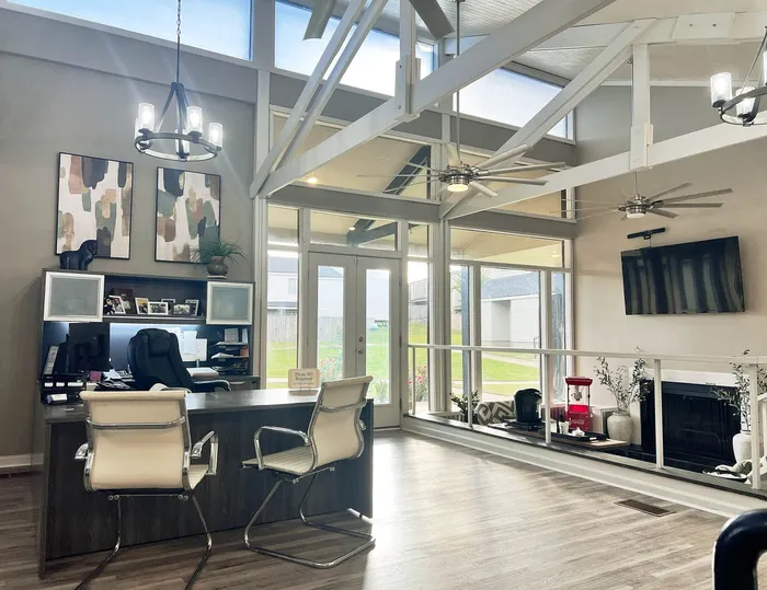 Bright, modern office space with high ceilings, stylish chandeliers, and an inviting seating area overlooking a garden view.