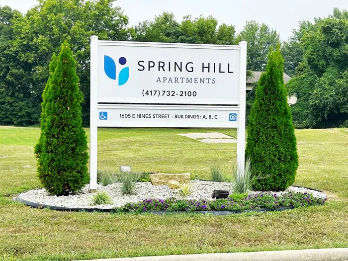 Inviting sign of Spring Hill Apartments set in a serene green landscape, highlighting accessibility and spacious living options in a tranquil environment.