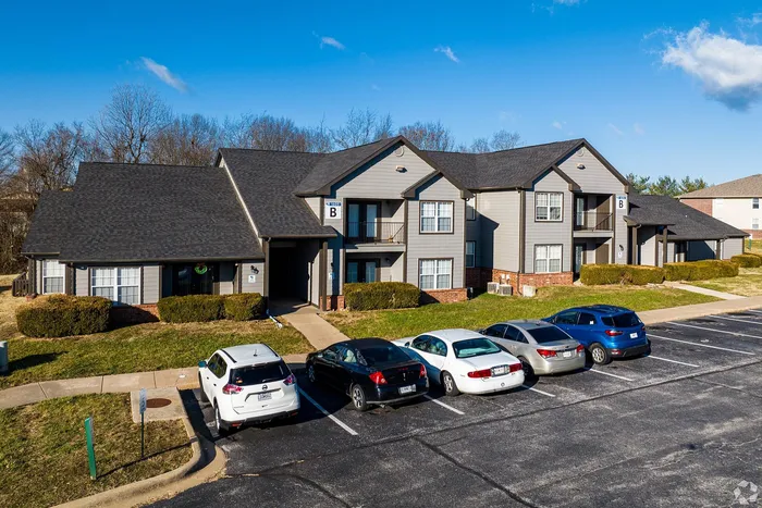Charming apartment complex with modern architecture, nestled in a serene neighborhood with ample parking space under a clear blue sky.