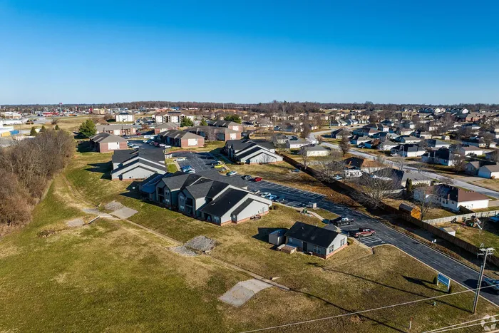 Expansive aerial view of a charming suburban neighborhood featuring modern apartment complexes surrounded by lush green spaces and wide streets.