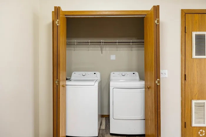 Convenient in-unit laundry area featuring modern washer and dryer with wooden closet doors.