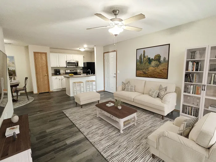 Inviting open-concept living area featuring a modern kitchen with white cabinets, cozy sofas, elegant bookshelf, and charming dining space.
