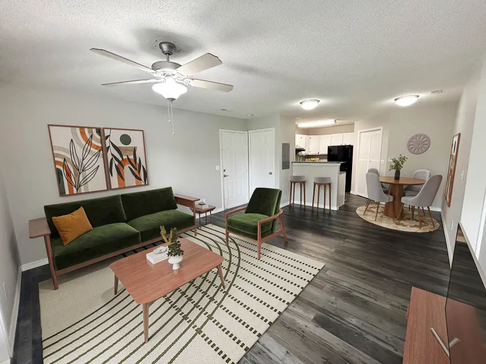 Modern living room with stylish green furniture, elegant wooden coffee table, and chic dining area, featuring a contemporary open kitchen.