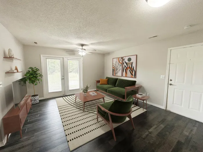 Bright living room with modern decor featuring a green sofa, chic artwork, and a stylish rug. Double doors open to a lush outdoor view.