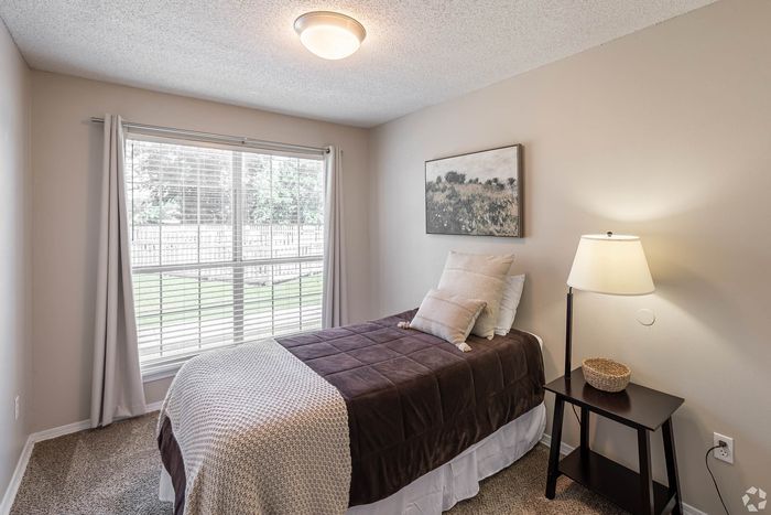 Cozy bedroom with a single bed, soft beige walls, a large window with garden view, and elegant lighting creating a serene atmosphere.