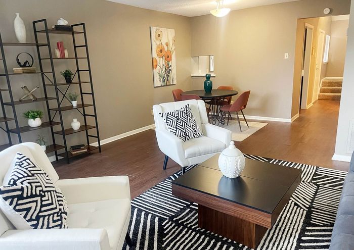Inviting living room with chic decor, featuring a stylish geometric rug, elegant white armchairs, and a cozy dining area with vibrant chairs, perfect for entertaining.