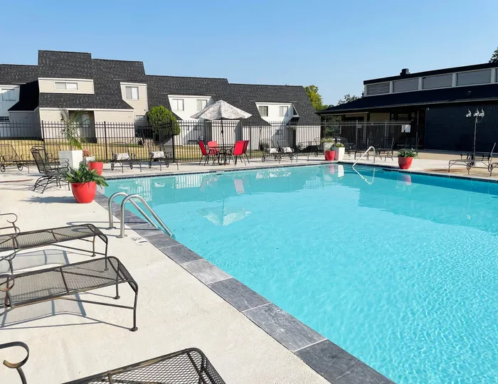 Inviting outdoor pool area with crystal-clear waters, surrounded by elegant lounge chairs and vibrant red planters for a relaxing ambiance.