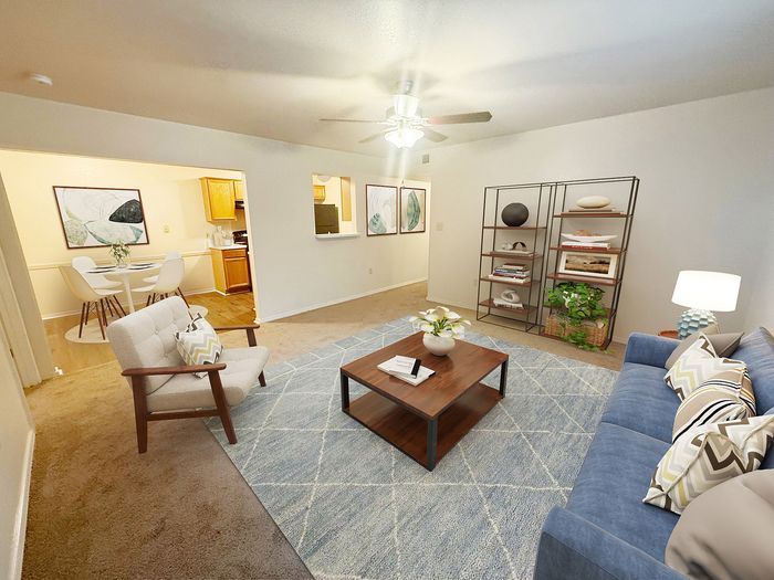 Inviting living room with modern decor and cozy seating, featuring a plush blue sofa and elegant armchair. Spacious open layout leads to a stylish dining area and warm-toned kitchen. Abundant natural light highlights the contemporary design, perfect for entertaining.