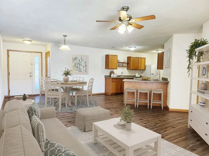 Inviting open-plan living space with cozy seating, elegant dining area, and modern kitchen with bar seating, enhanced by warm wood floors and bright lighting.