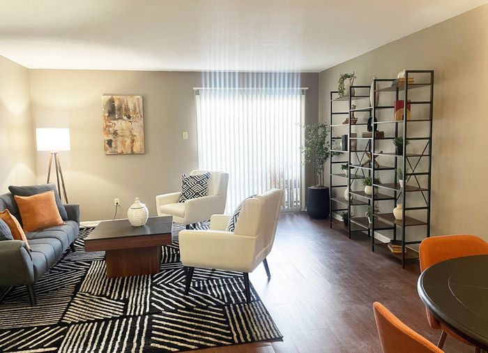 Chic living room with modern decor, featuring a cozy sofa, stylish armchairs, and a patterned rug, complemented by a bookshelf with decorative accents and natural light streaming through large windows.