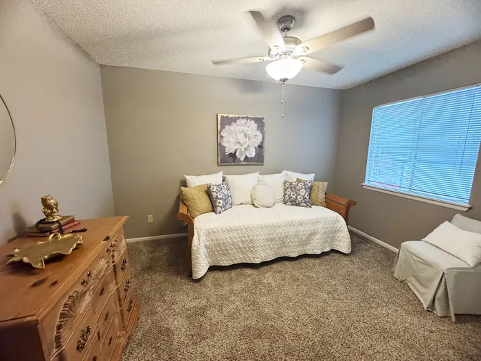 Cozy bedroom featuring a stylish daybed with elegant cushions, warm wooden dresser, and soft carpet flooring for ultimate comfort.
