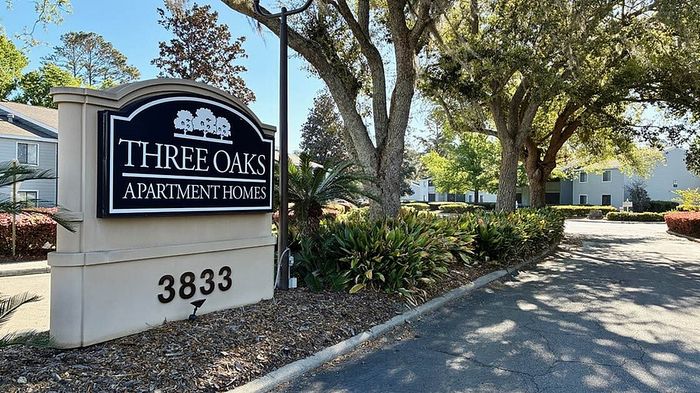 Charming entrance to Three Oaks Apartment Homes, highlighted by lush greenery and mature trees for a serene living atmosphere.
