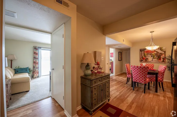 Cozy apartment interior featuring a chic dining area with vibrant red patterned chairs, a comfortable living space with plush beige seating, and elegant decor accented by warm wooden flooring.