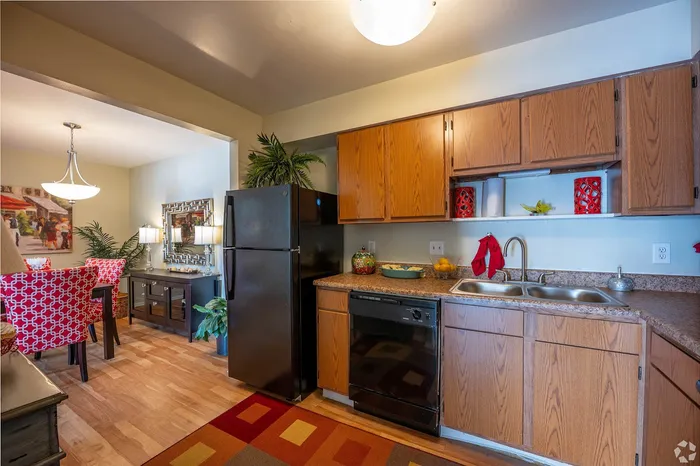 Charming apartment kitchen with sleek black appliances, warm wooden cabinetry, and a vibrant dining area with stylish red chairs.