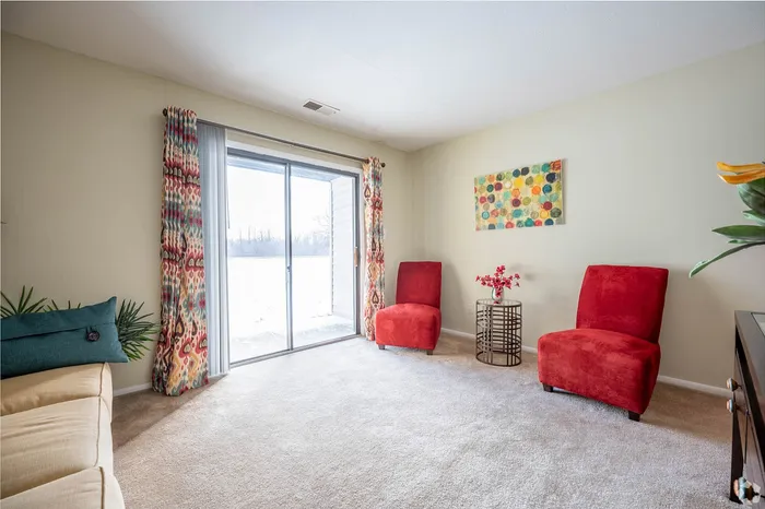 Bright and inviting living room with red chairs, abstract art, and large sliding glass doors offering a serene view.