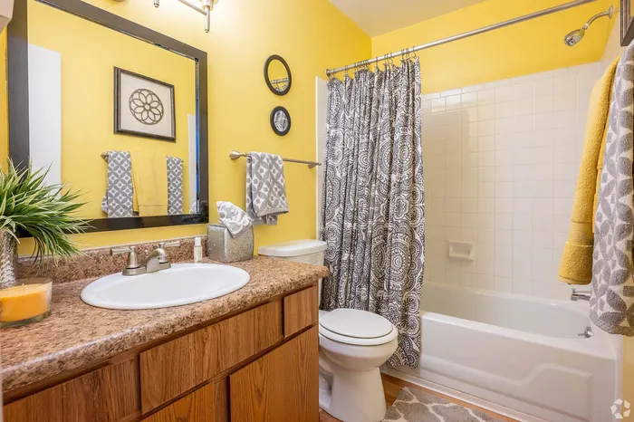 Vibrant bathroom with stylish decor, featuring a yellow accent wall, patterned shower curtain, and elegant vanity.