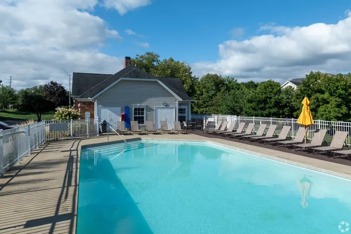 Inviting outdoor pool area with sun loungers and charming clubhouse surrounded by lush greenery, perfect for relaxation and leisure.