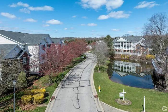 Charming apartment community with serene pond views, lush landscaping, and tree-lined street under a bright blue sky.