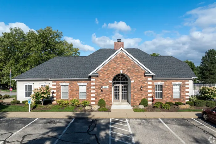 Charming brick building with manicured landscaping, showcasing a welcoming entrance and ample parking under a bright blue sky.