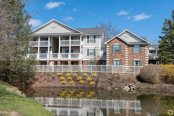 Charming apartment complex with spacious balconies, surrounded by lush greenery and overlooking a serene pond.