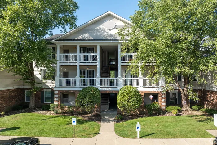 Charming apartment building with classic white balconies and lush green landscaping, offering a welcoming entrance and spacious living.