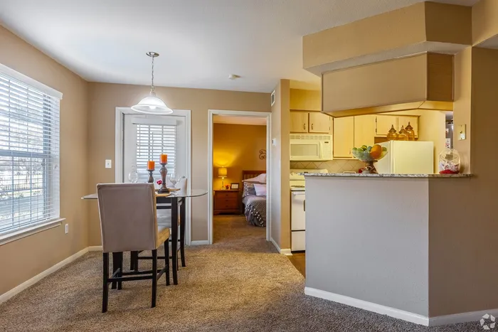 Charming apartment dining area with natural light, adjacent to a cozy bedroom and a modern kitchen featuring warm tones and elegant decor.