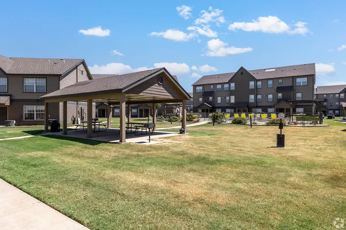 Spacious apartment complex with charming gazebo, manicured lawns, and picnic areas under a clear blue sky.