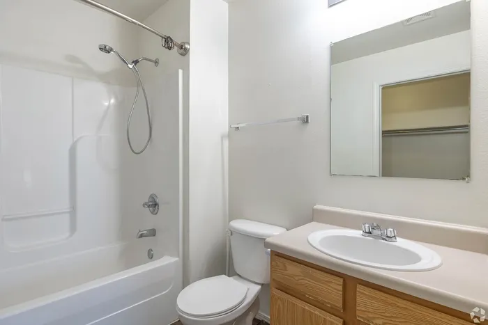Bright and modern bathroom featuring a sleek vanity, spacious mirror, and a pristine bathtub with shower fixtures.
