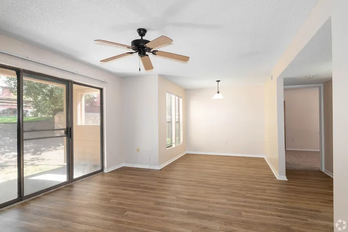 Bright living area with sleek hardwood floors, ceiling fan, and sliding doors leading to a sunlit patio.