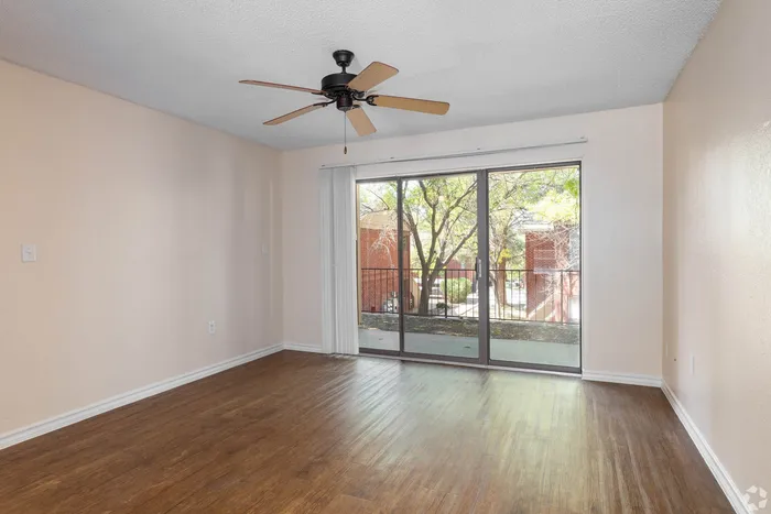 Bright, spacious room with elegant hardwood floors, ceiling fan, and large sliding glass doors opening to a serene view.