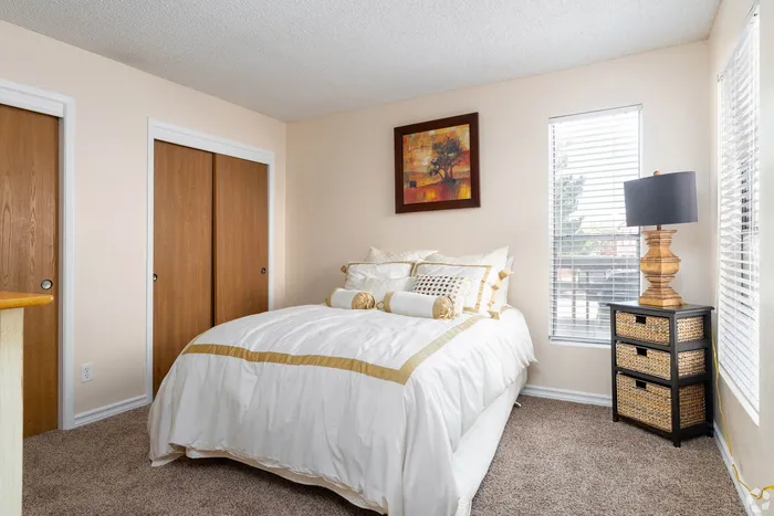 Inviting bedroom with cozy white bedding, elegant wall art, and ample natural light from large windows.