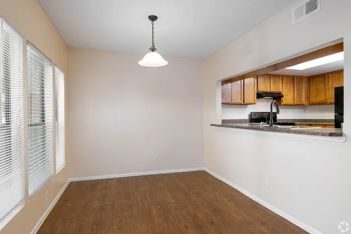 Inviting modern dining area with elegant pendant lighting, warm wood flooring, and a stylish kitchen pass-through with rich wood cabinetry.