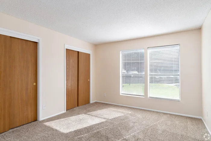 Bright and airy bedroom with large windows, plush carpeting, and dual wooden closets, perfect for a cozy and organized living space.