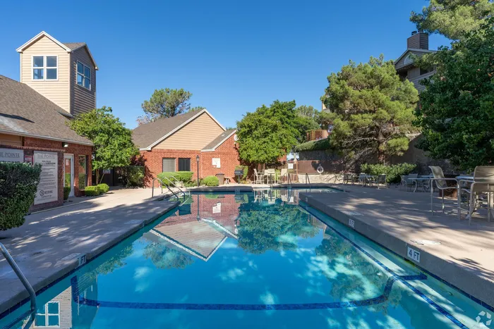Inviting community pool area with clear blue water, surrounded by lush greenery and cozy seating, ideal for relaxation and outdoor enjoyment.