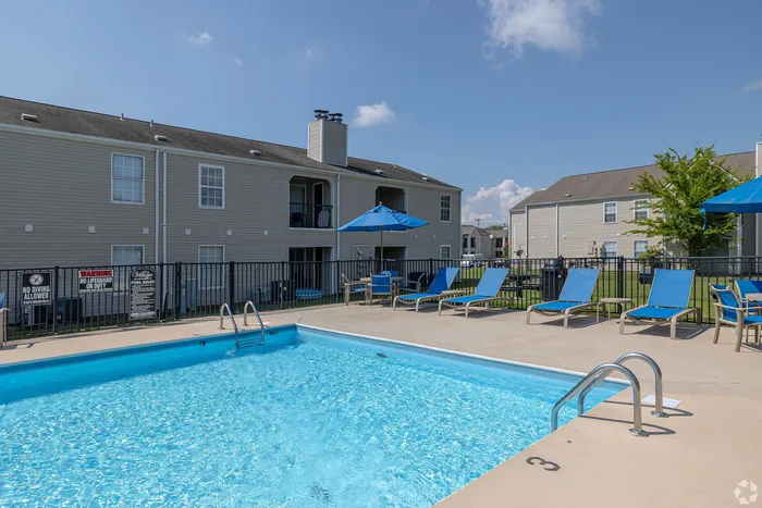 Inviting apartment community pool with comfortable loungers and blue umbrellas, offering a relaxing outdoor experience.