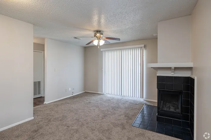 Cozy living room featuring plush carpeting, a modern ceiling fan, and a chic tiled fireplace accentuated by natural light streaming through vertical blinds.