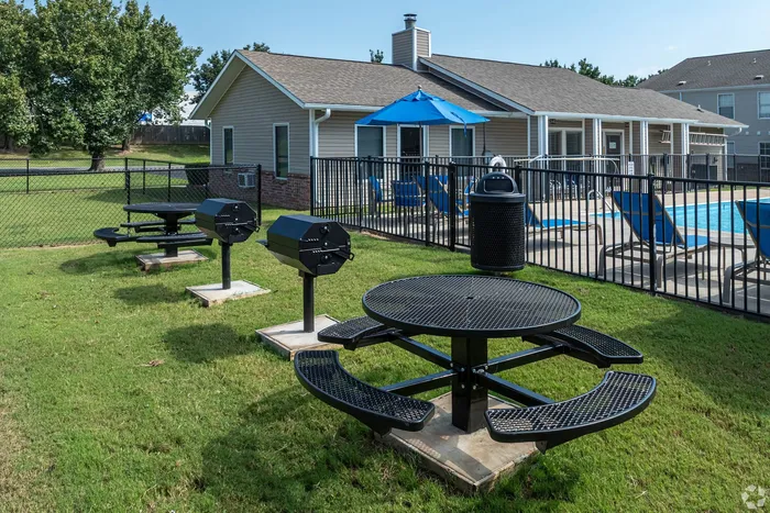 Inviting outdoor area with barbecue grills, picnic tables, and a refreshing poolside retreat adorned with blue lounge chairs and umbrellas.