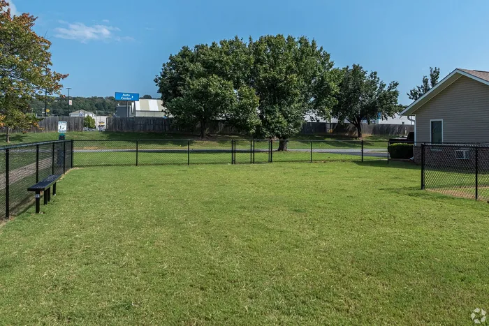Charming residential backyard featuring lush green lawns, fenced area, and mature trees under a bright blue sky.