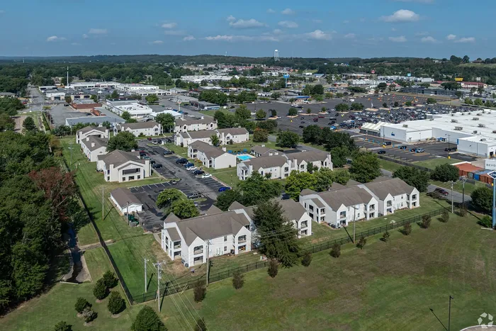 Picturesque aerial view of a charming apartment complex nestled in lush greenery, featuring modern design and ample parking, with convenient access to nearby shopping and amenities.