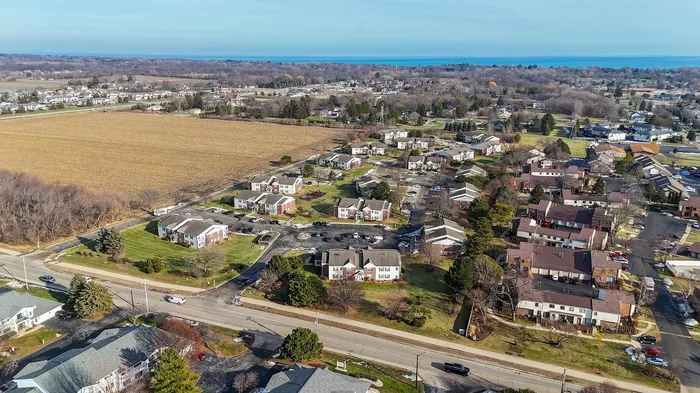 Scenic aerial view of a spacious apartment community surrounded by lush greenery and open fields, offering a peaceful suburban lifestyle.