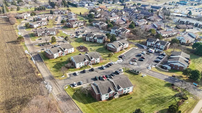 Aerial view of a charming residential community showcasing spacious green lawns, modern apartment buildings, and ample parking areas in a serene suburban setting.