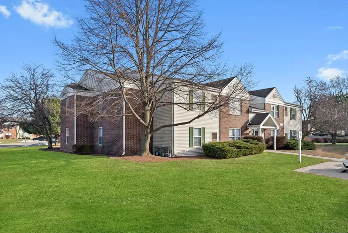Charming apartment exterior with brick facade and lush green lawn, offering a tranquil suburban setting.