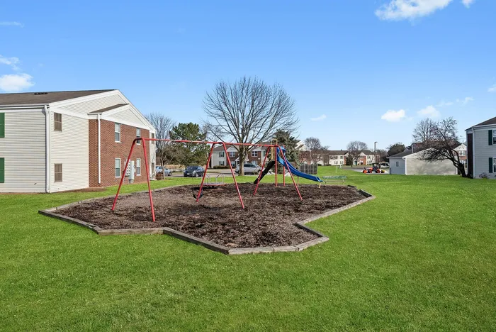 Inviting outdoor playground with swings and a slide surrounded by lush green lawns in a friendly residential neighborhood.