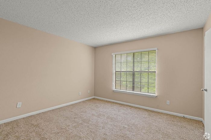 Bright and airy room featuring plush carpet, neutral walls, and a large window with wooden blinds offering picturesque outdoor views.